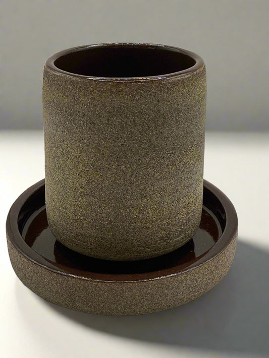 Brown ceramic cup with matching saucer on a white background