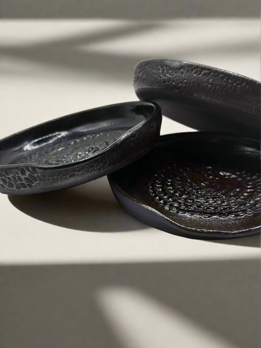 Three black ceramic dishes with textured surface on a white background
