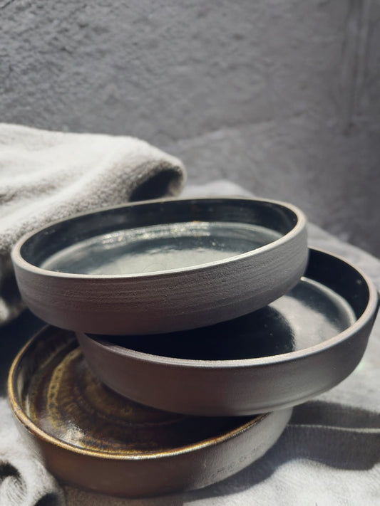 Stack of black ceramic bowls on a textured surface with a gray background