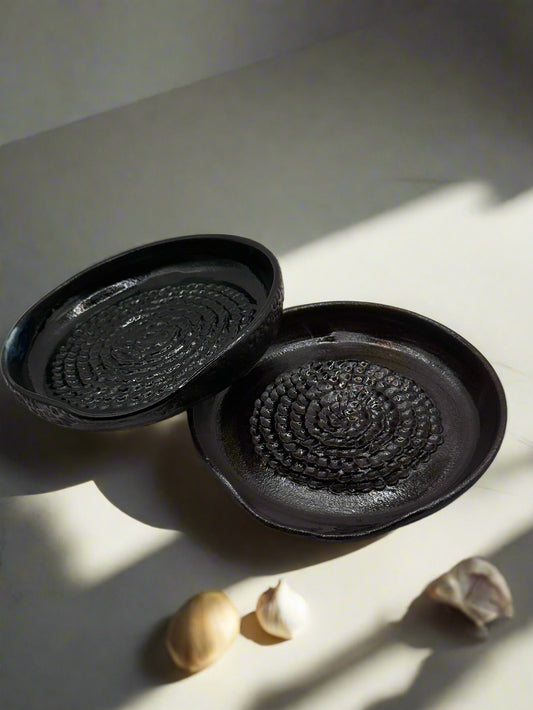 Two black ceramic coasters with textured surface on a white background