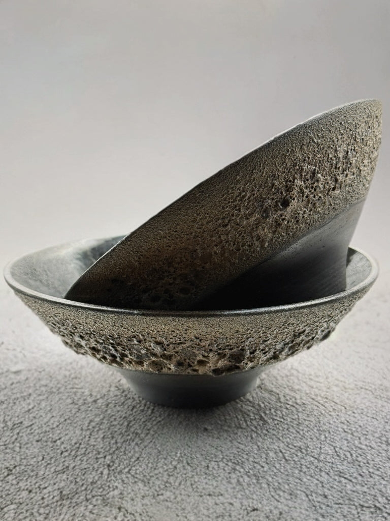 Two textured ceramic bowls stacked on a gray surface