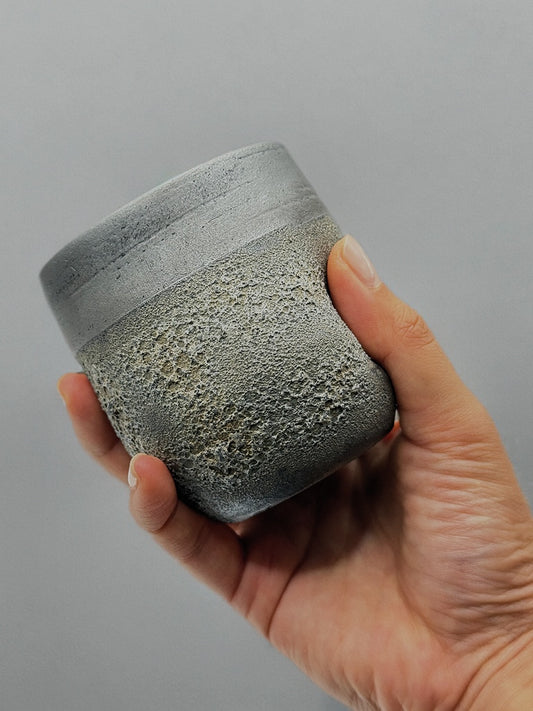 Hand holding a textured gray ceramic cup against a plain background